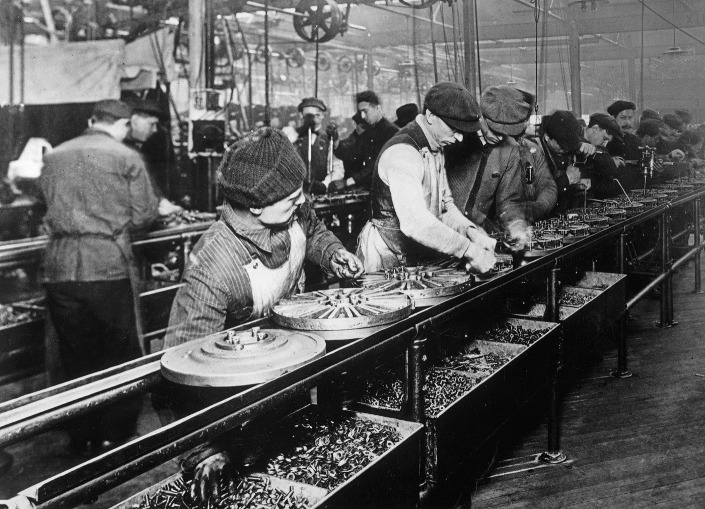 Workers on Ford's 1913 moving assembly line, assembling magnetos in a long uniform row.