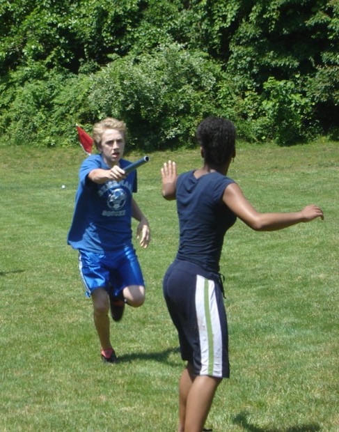 Two relay runners mid-exchange, one reaching back and one reaching forward to pass a baton.