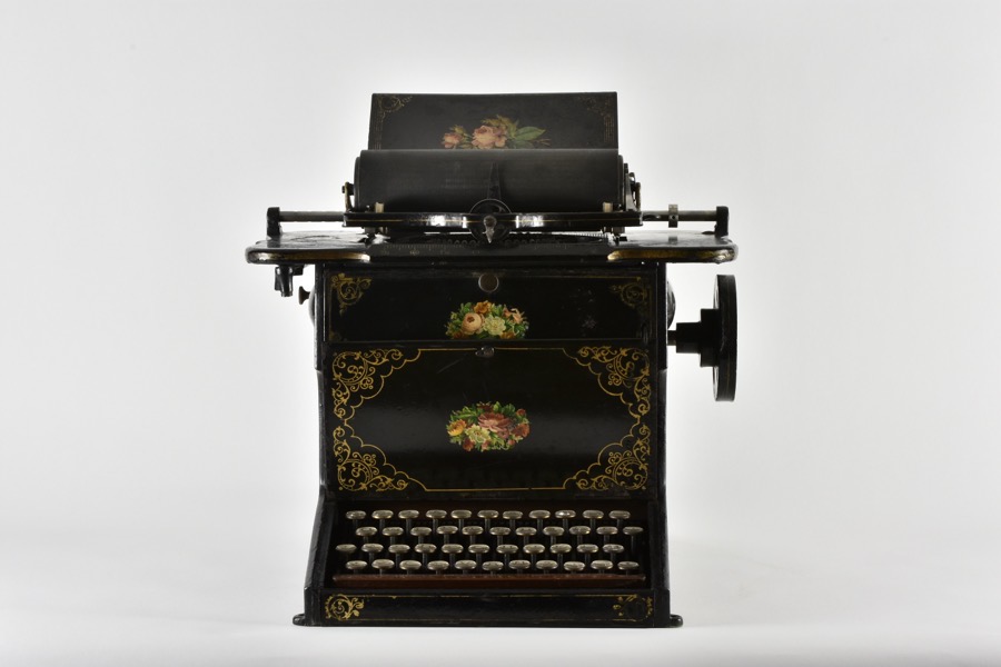 An ornately decorated Sholes and Glidden Typewriter from 1873, with a circular fan of keys below its carriage.